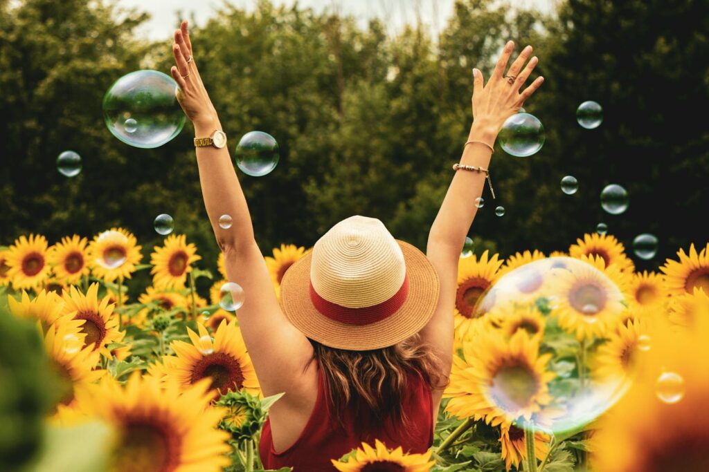 Photo by Andre Furtado A joyful woman in a sunflower field with bubbles, expressing happiness on a summer day.